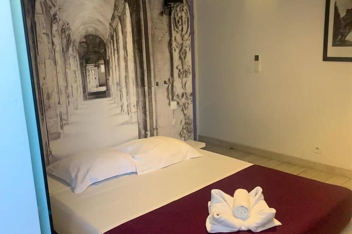 A hotel room with a bed, a red blanket, and a towel on the bed.
