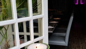 Una vela verde en un marco blanco de ventana, un suelo de madera y una zona de estar con mesa y sillas.