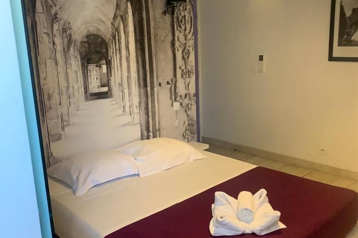A hotel room with a bed, a red blanket, and a towel on the bed.