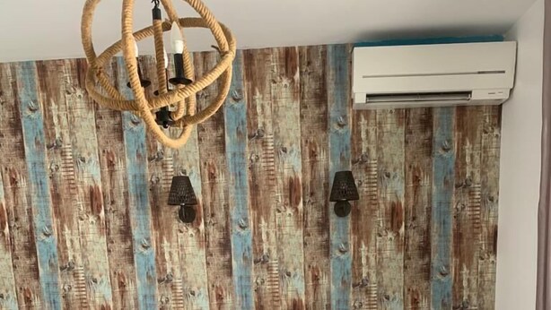 Habitación de hotel con cama, candelabro, equipo de aire acondicionado y una pared con diseño de madera.