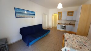 Un espace de vie compact comprenant un canapé, une kitchenette et un tableau représentant une scène de plage.