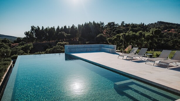 Una piscina infinita azul cristalina con sillones de descanso y vistas a un paisaje montañoso.
