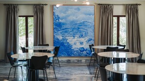 Un comedor con mesas y sillas redondas, un cuadro grande en la pared y cortinas en las ventanas.