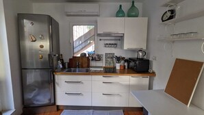 A compact kitchen with a stainless steel refrigerator, white cabinets, a wooden countertop, and a window providing natural light.