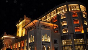 Un edificio grande e histórico con múltiples ventanales arqueados y balcones, iluminado por la noche.