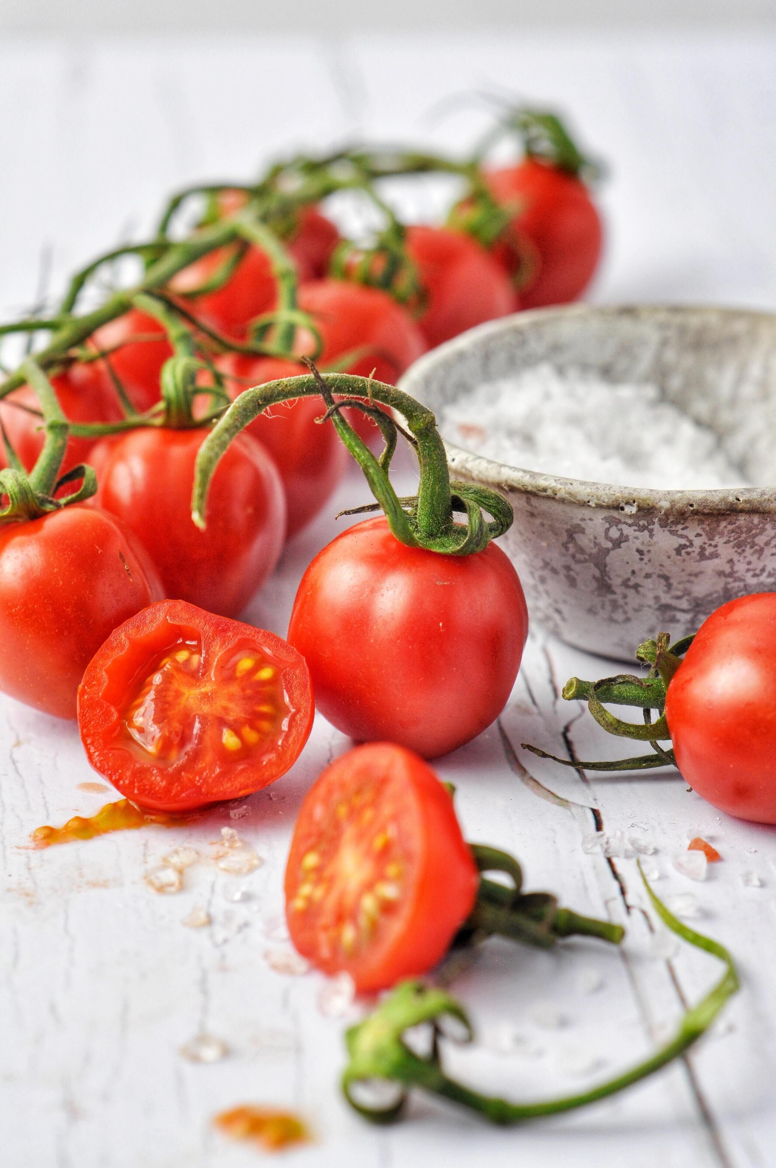 Tomatoes on the vine with a bowl of salt nearby.