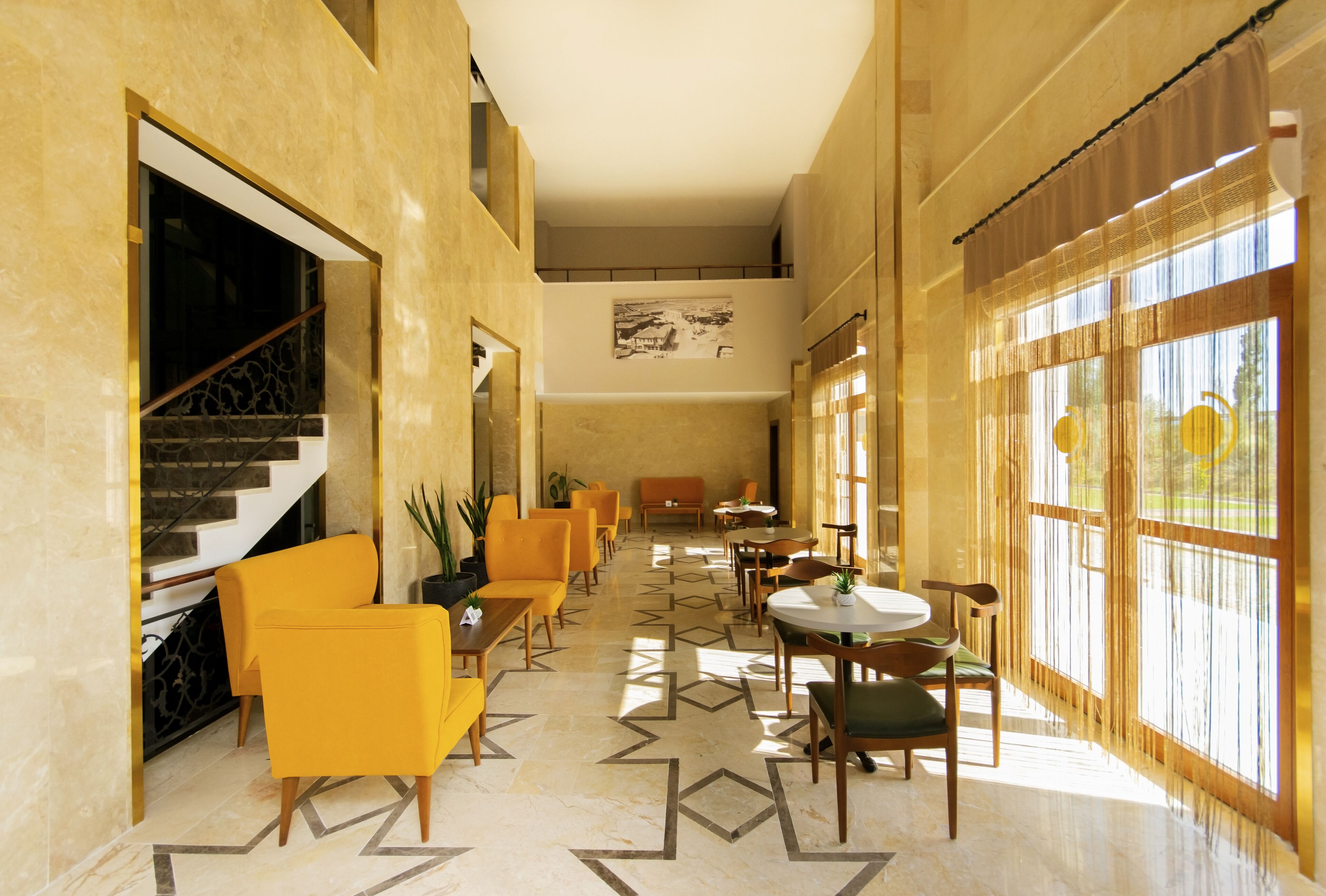 A spacious lobby with a geometric patterned floor, modern yellow chairs, and a staircase.
