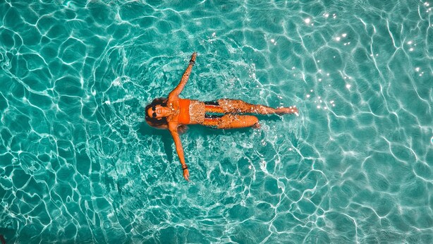 Una persona flota en una piscina azul cristalina con reflejos y ondulaciones.