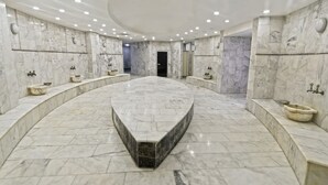 Un baño espacioso con piso de mármol curvo, varios lavamanos y un lavatrastos central de mármol.