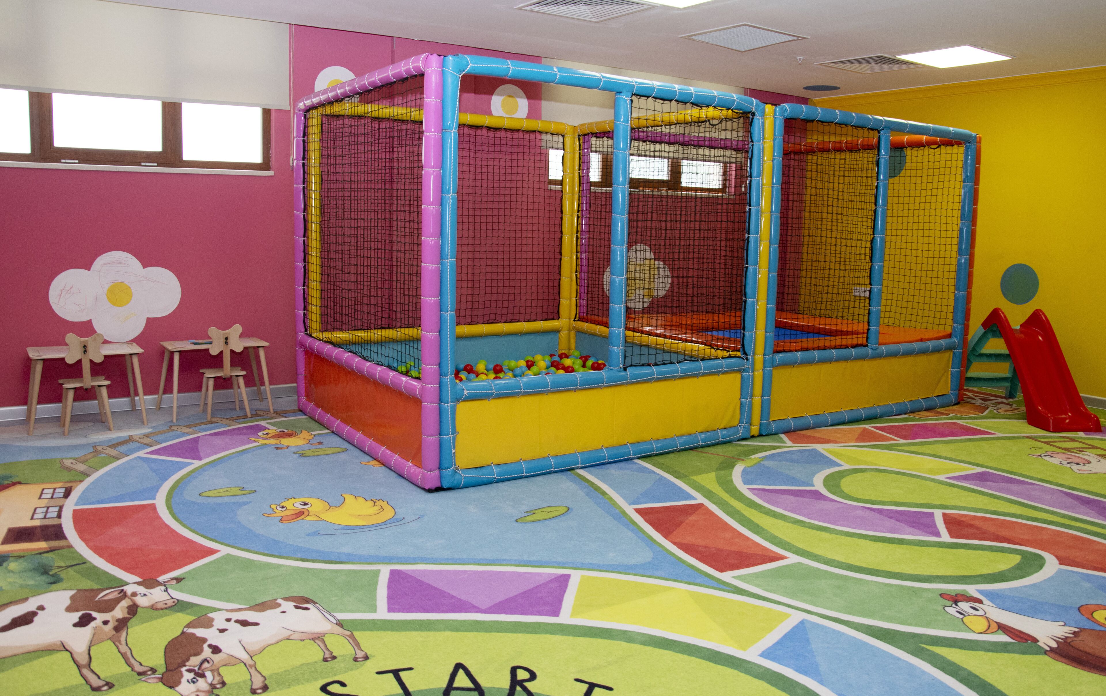Un área de juegos con un corralito colorido, una piscina de pelotas y un tobogán.