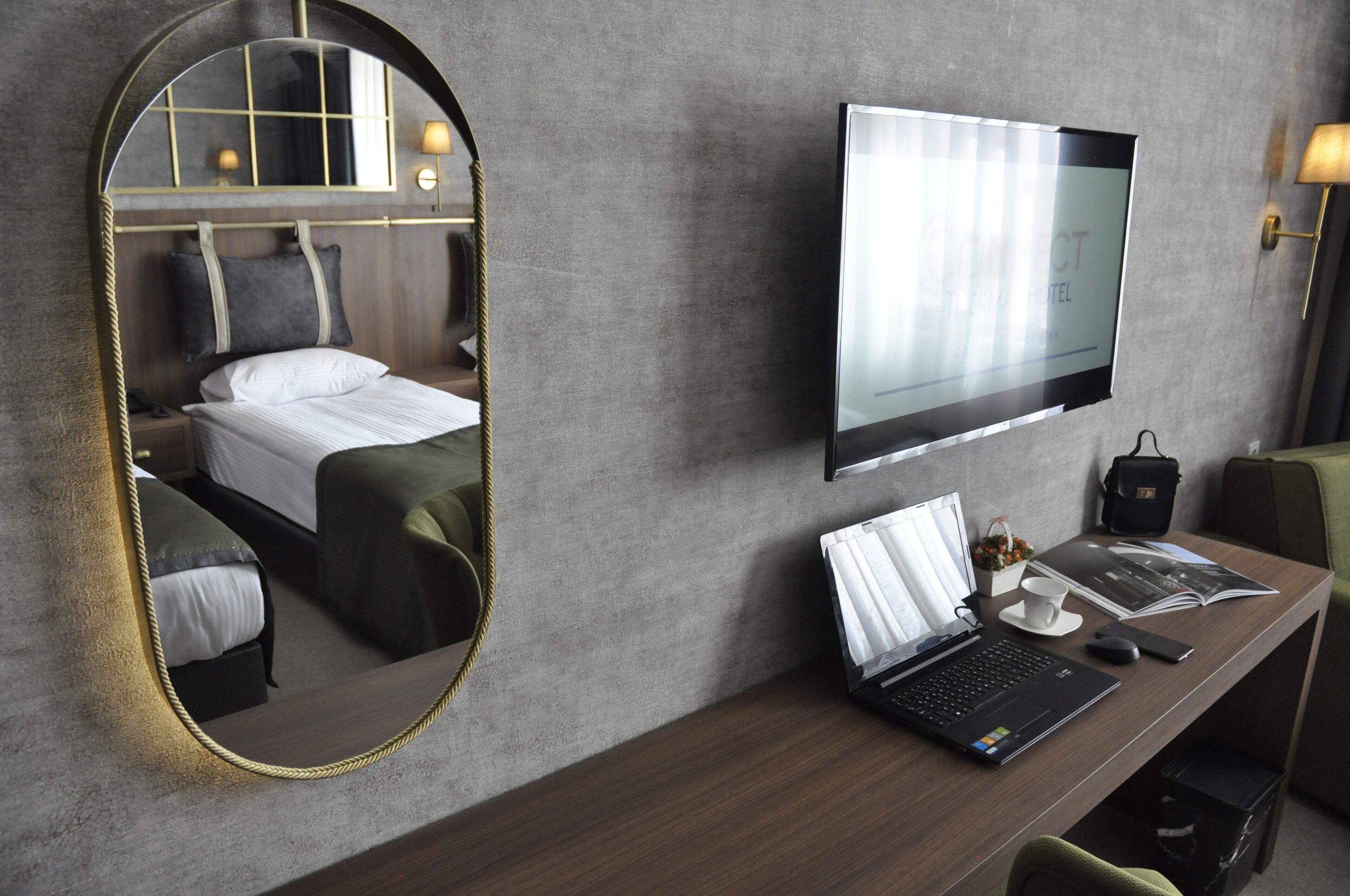 Habitación de hotel con cama, escritorio, computadora portátil, televisor y espejo.