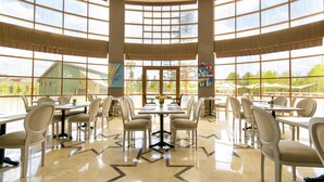 Un comedor amplio con varias mesas y sillas, ventanas grandes y vistas al exterior.