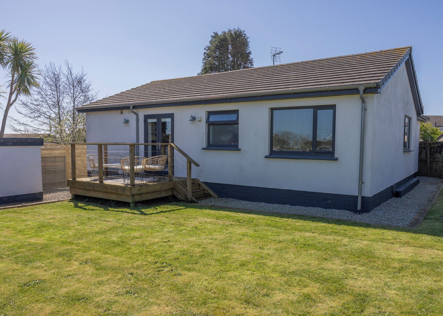 Ein Bungalow mit einer Terrasse, einer kleinen Veranda und einem eingezäunten Garten.