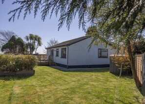 A single-story house with a small deck, surrounded by a well-maintained lawn and various trees. - 38 Venn Park (Dartmouth)
