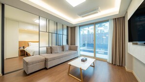 A modern living room with a sofa, ottoman, and coffee table. There is a large window with curtains and a view of the outside. - Chungchoho Best Hotel (Sokcho)