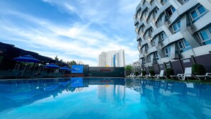 A swimming pool with lounge chairs, a covered area with umbrellas, and a modern building with balconies. - Chungchoho Best Hotel (Sokcho)