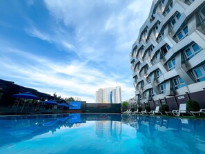 A swimming pool with lounge chairs, a covered area with umbrellas, and a modern building with balconies. - Chungchoho Best Hotel (Sokcho)