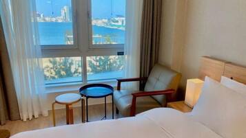 Ein Hotelzimmer mit Bett, einem kleinen Tisch, einem Stuhl und Blick auf das Meer und Gebäude.