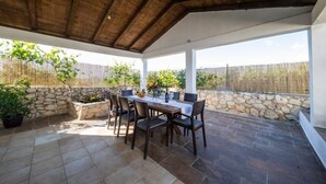 A covered patio area with a stone wall, a table with chairs, and potted plants. - Summer House Amon (Razanac)