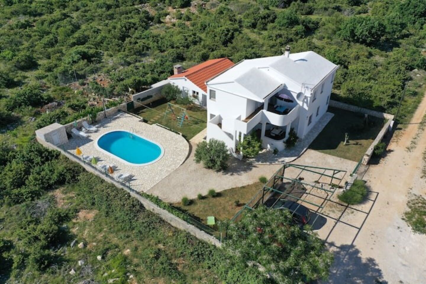 A white villa with a swimming pool, surrounded by greenery.