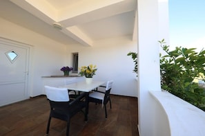 A small, enclosed patio area with a table and chairs, a potted plant, and a door with a window. - Summer House Amon (Razanac)