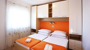 A hotel room with two beds, a window with sheer curtains, and white cabinets with orange accents. - Summer House Amon (Razanac)