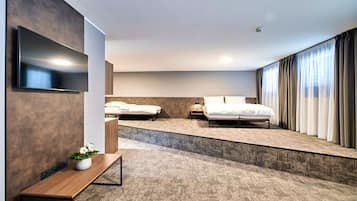 A modern hotel room with two beds, a flat-screen TV, a small table with a plant, and a large window with curtains.