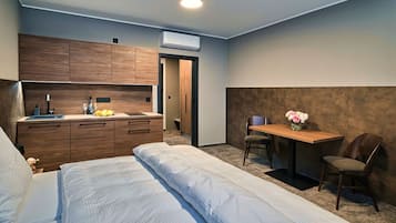 Ein kompaktes Hotelzimmer mit einem Bett, einer kleinen Küchenzeile, einem Schreibtisch mit Stuhl und einer Wand-Klimaanlage.