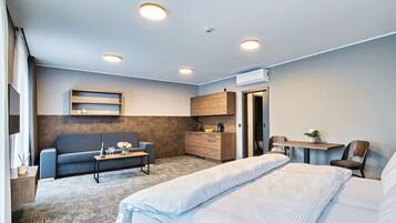 A modern hotel room with a sofa, a bed, a small kitchenette, and a desk.