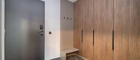 Una habitación con una puerta gris, un banco y un armario de madera con pomos negros.