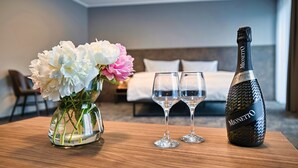 Habitación de hotel con una cama, un jarrón de flores y dos copas junto a una botella de Monetto champagne.