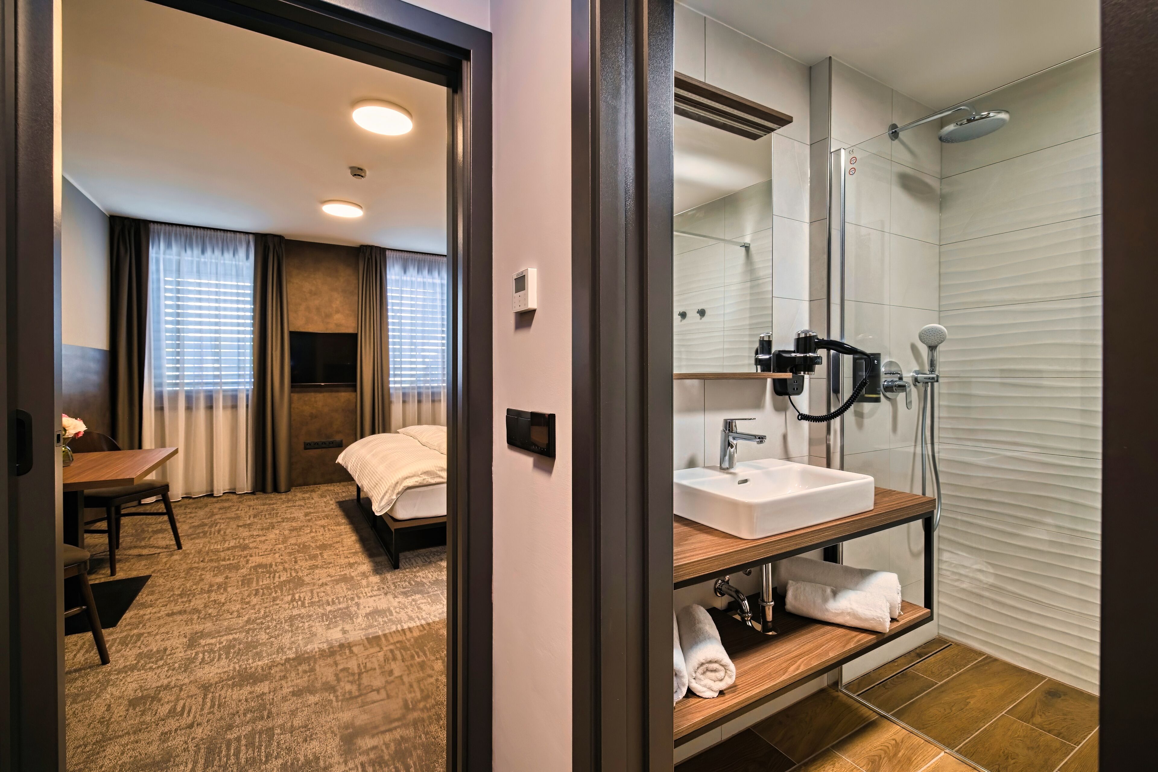 Una habitación de hotel con cama, escritorio, baño con lavabo y ducha, y espejo.