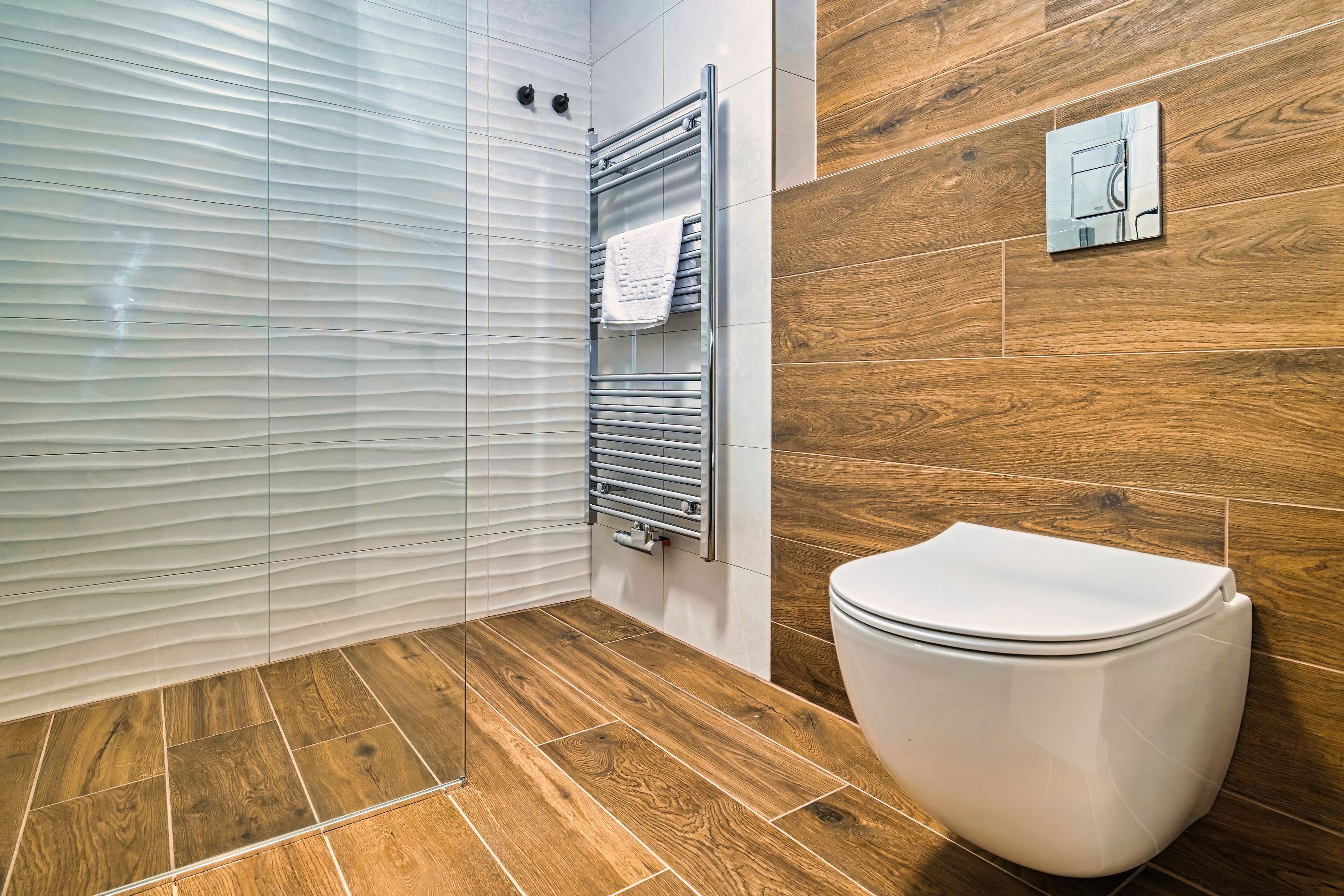 A modern bathroom with a wooden floor, a white toilet, a towel rack, and a glass shower enclosure.