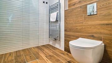 A modern bathroom with a wooden floor, a white toilet, a towel rack, and a glass shower enclosure.