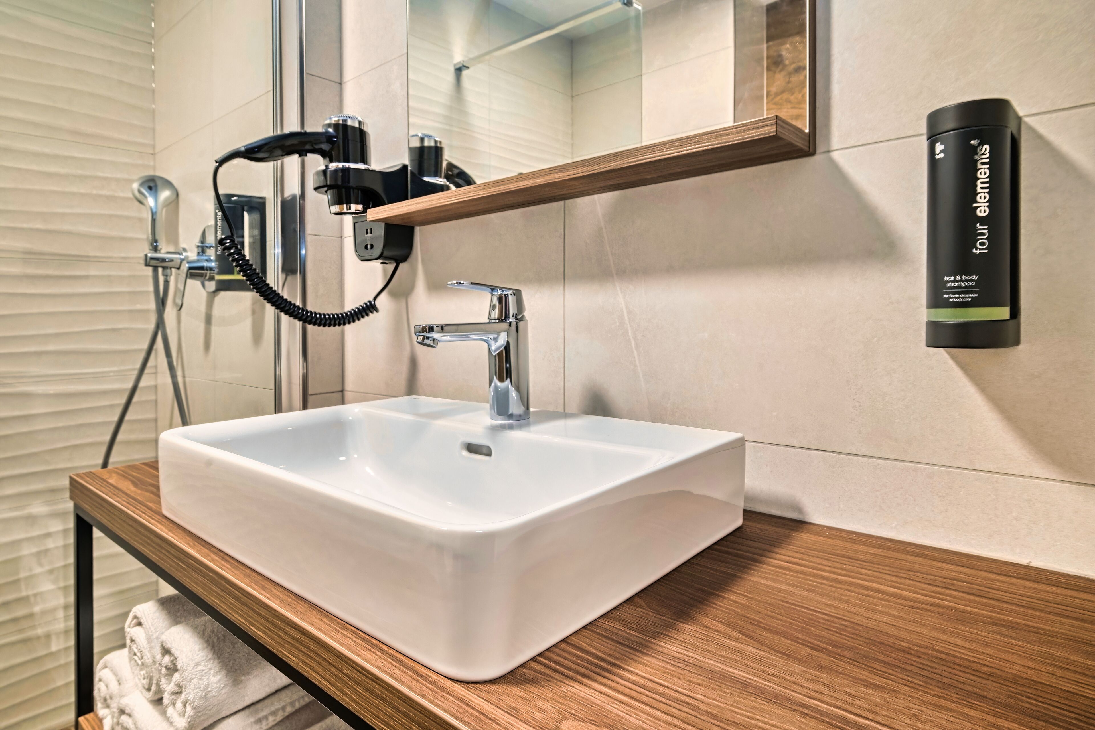 A bathroom with a white sink, a wooden vanity, a mirror, a towel rack, and a hand dryer.