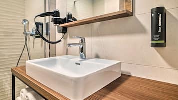 A bathroom with a white sink, a wooden vanity, a mirror, a towel rack, and a hand dryer.