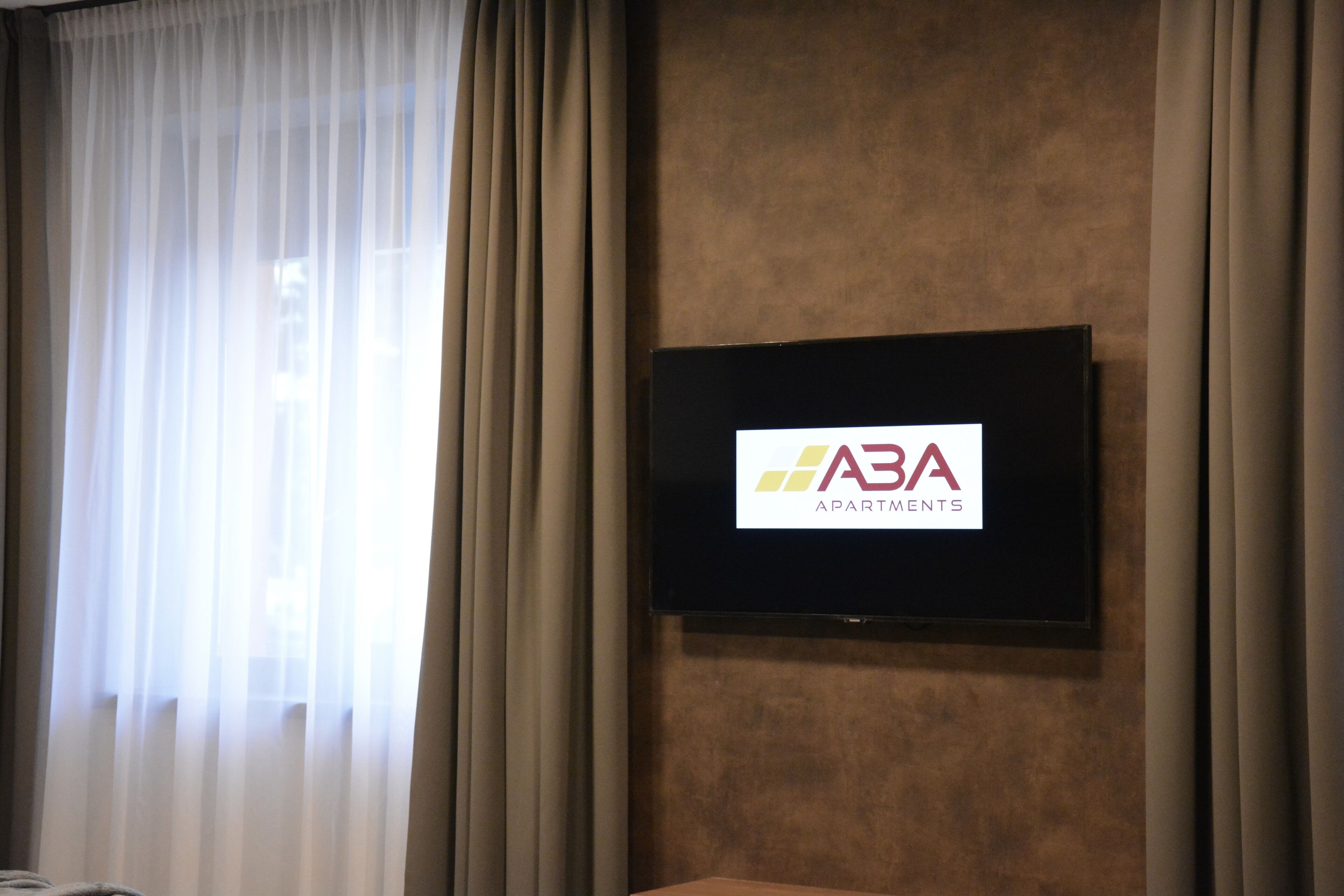 A flat-screen TV mounted on a wall with a logo for 'ABA Apartments'.