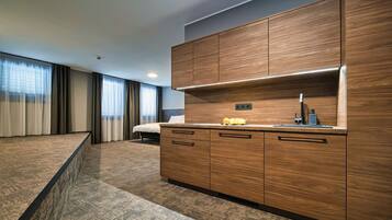 A modern hotel room with a wooden kitchenette, a bed, and a large window with curtains.
