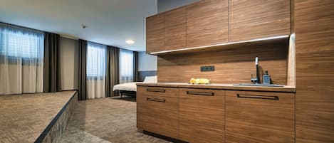 Una habitación de hotel moderna con una pequeña cocina de madera, una cama y un ventanal con cortinas.