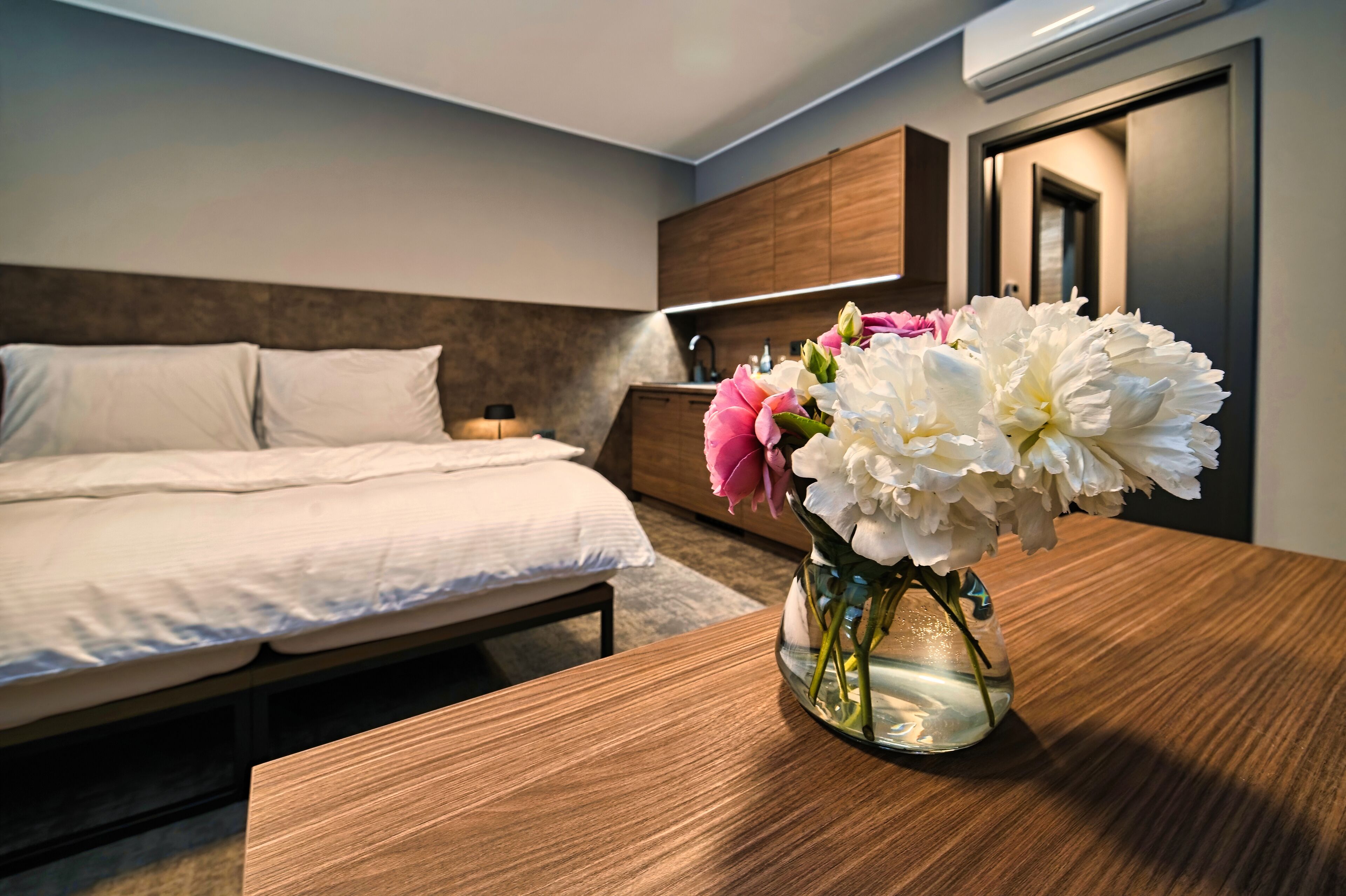 A hotel room with a bed, bedside table, and a vase of flowers.
