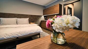 A hotel room with a bed, bedside table, and a vase of flowers.