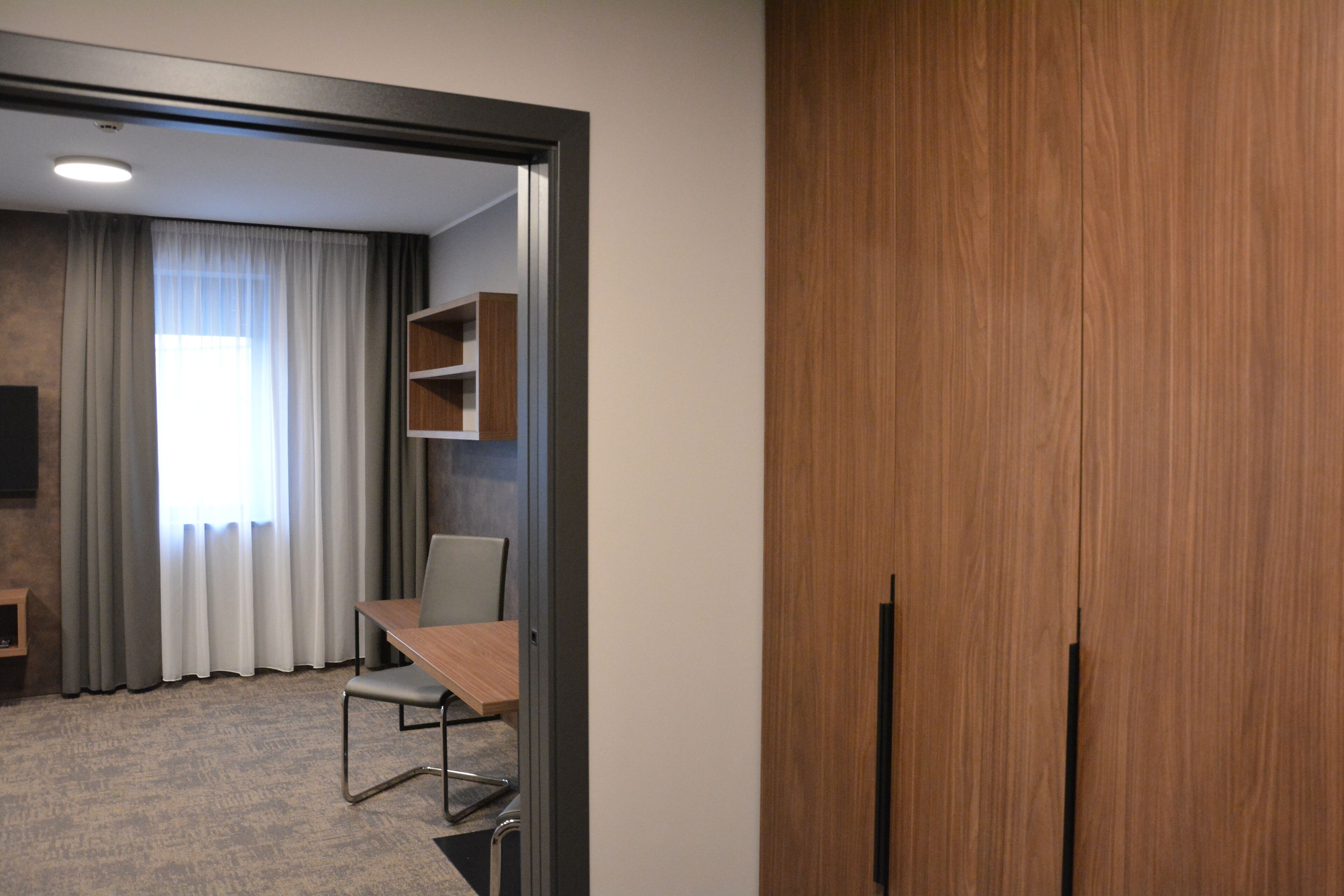 Ein Hotelzimmer mit Holzschrank, Schreibtisch mit Stuhl, Fernseher und einem Fenster mit Vorhängen.