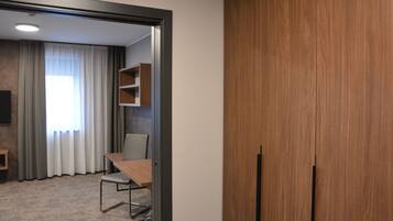 Ein Hotelzimmer mit Holzschrank, Schreibtisch mit Stuhl, Fernseher und einem Fenster mit Vorhängen.