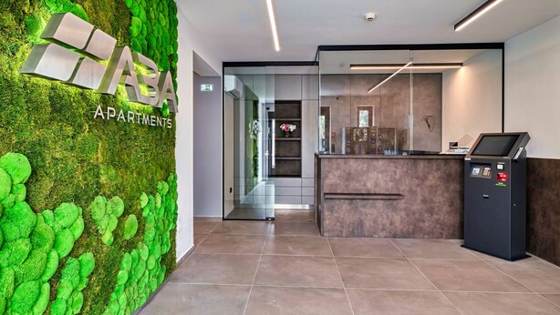 Un área de recepción con una pared cubierta de musgo verde, un mostrador de recepción y una decoración interior moderna.