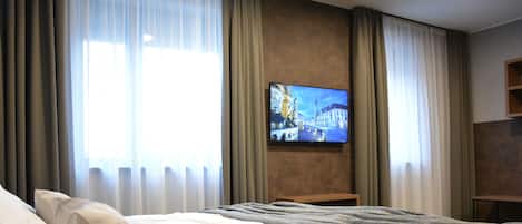 Habitación de hotel con una cama grande, un televisor de pantalla plana en la pared y una ventana con cortinas.