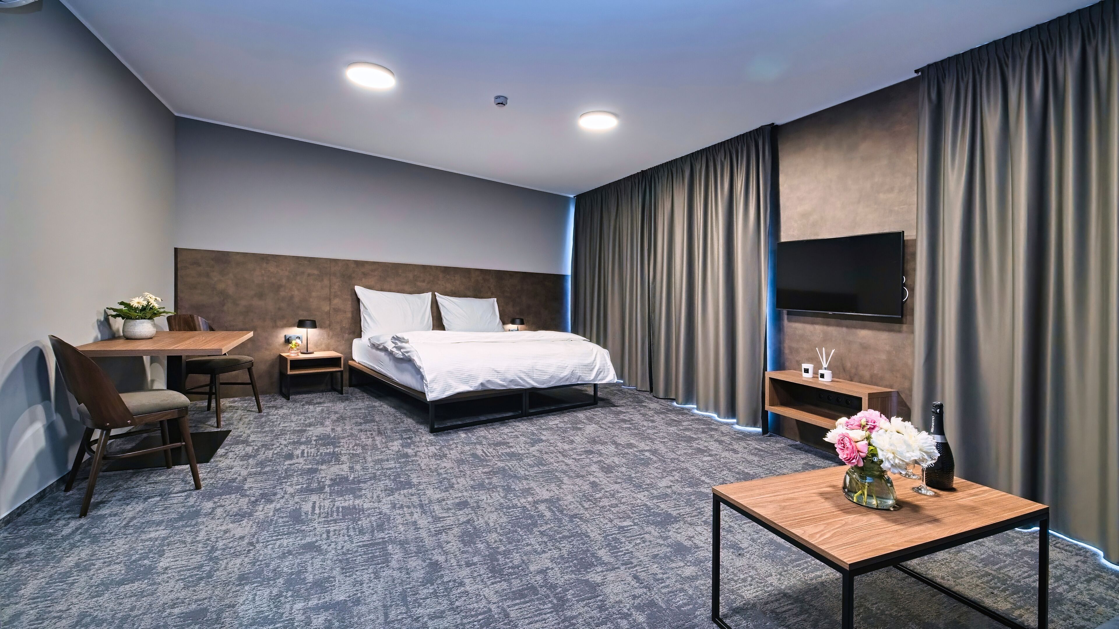 Een hotelkamer met een bed, een bureau, een stoel, een televisie en een kleine tafel met bloemen.