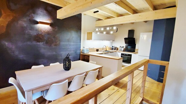 Una cucina moderna con travi in legno, un'area pranzo con sedie bianche e un oggetto decorativo nero sul tavolo.
