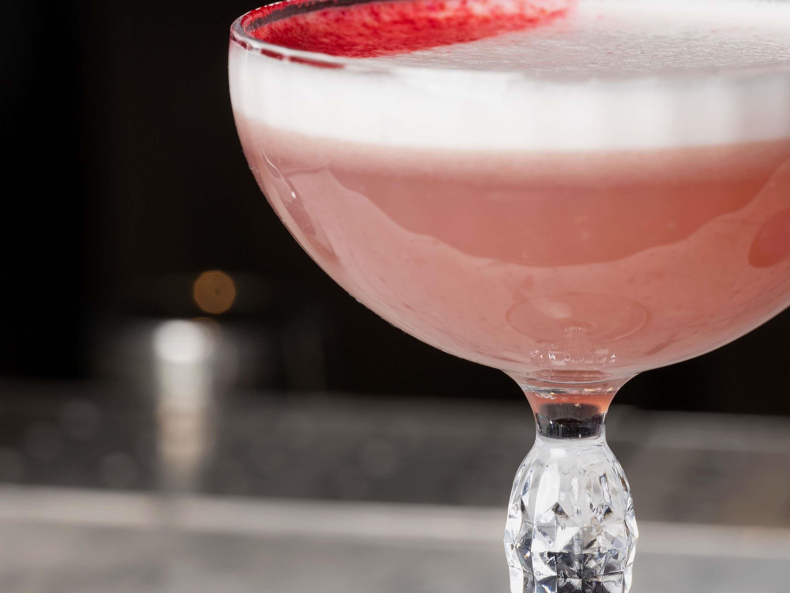 A cocktail in a clear glass with a red rim.