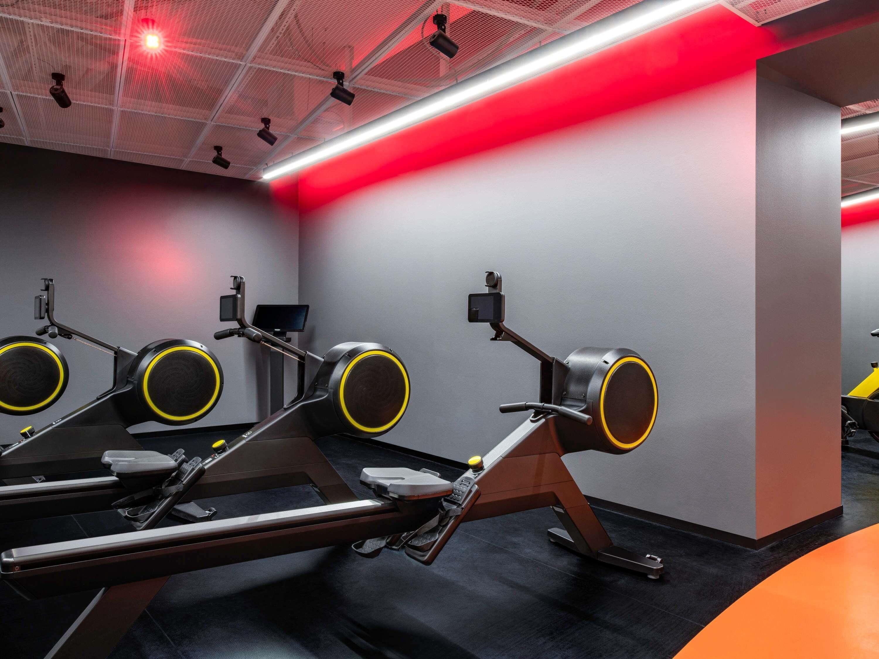A gym with exercise equipment, a digital screen, and a red-lit ceiling.