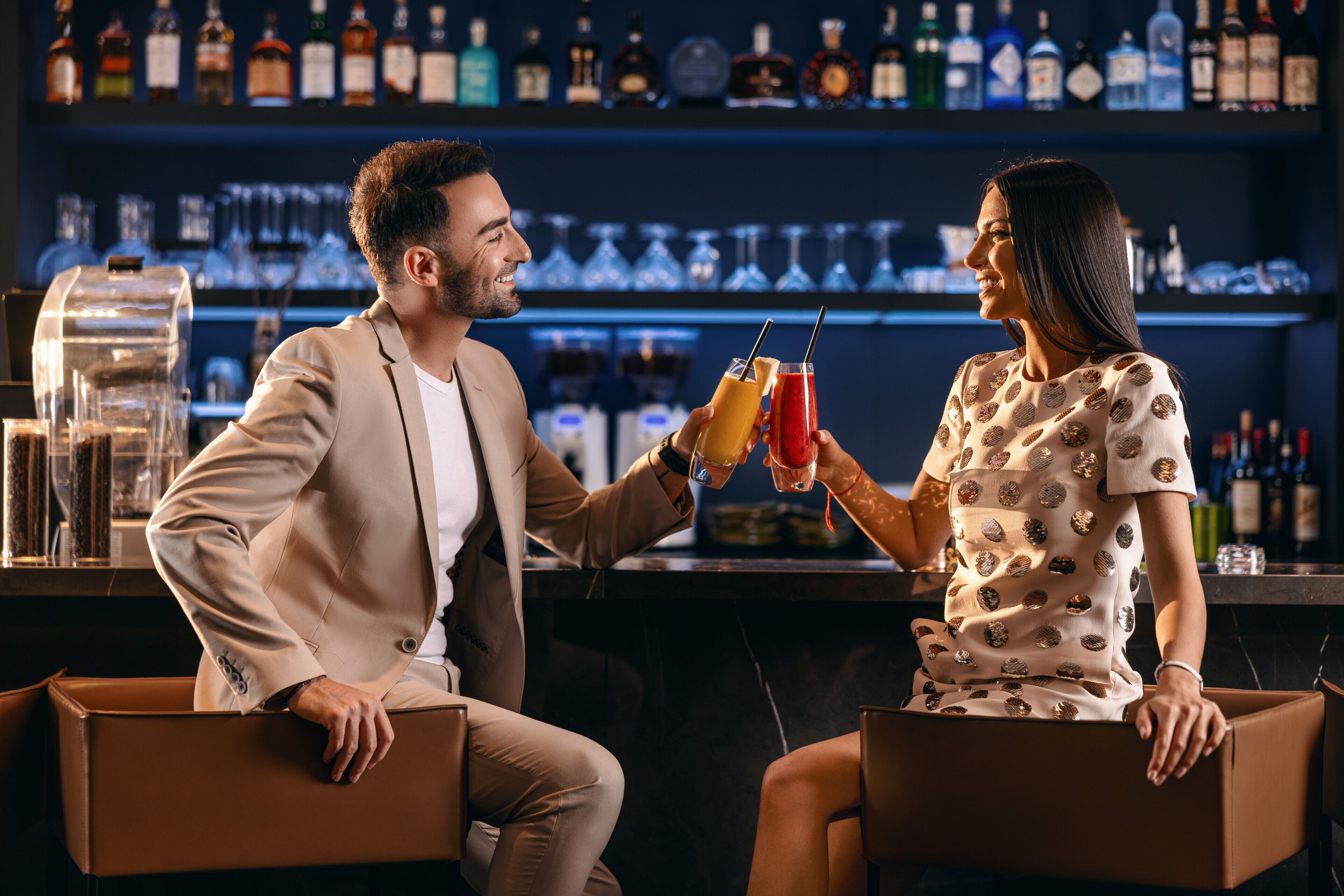Deux personnes sont assises au bar, et on peut voir une variété de bouteilles en arrière-plan.